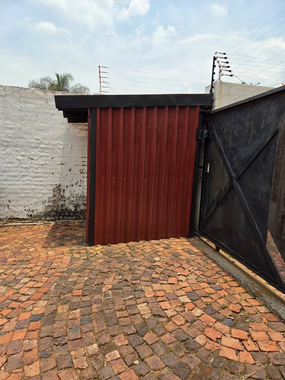 Custom red sliding gate on a cobblestone driveway
